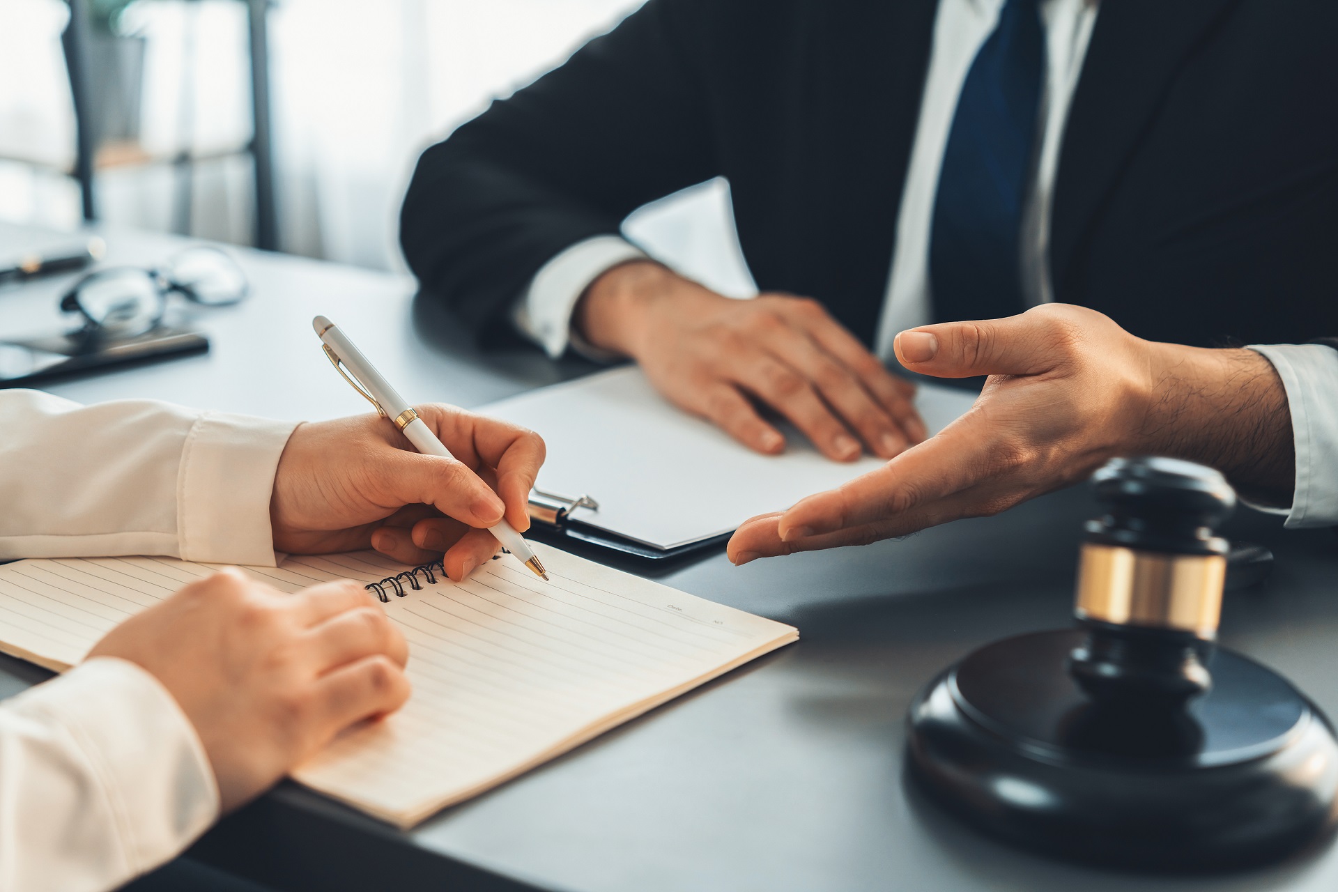 Two professionals review and sign documents during a legal or business meeting, with a judge's gavel in the foreground symbolizing legal proceedings or dispute resolution.