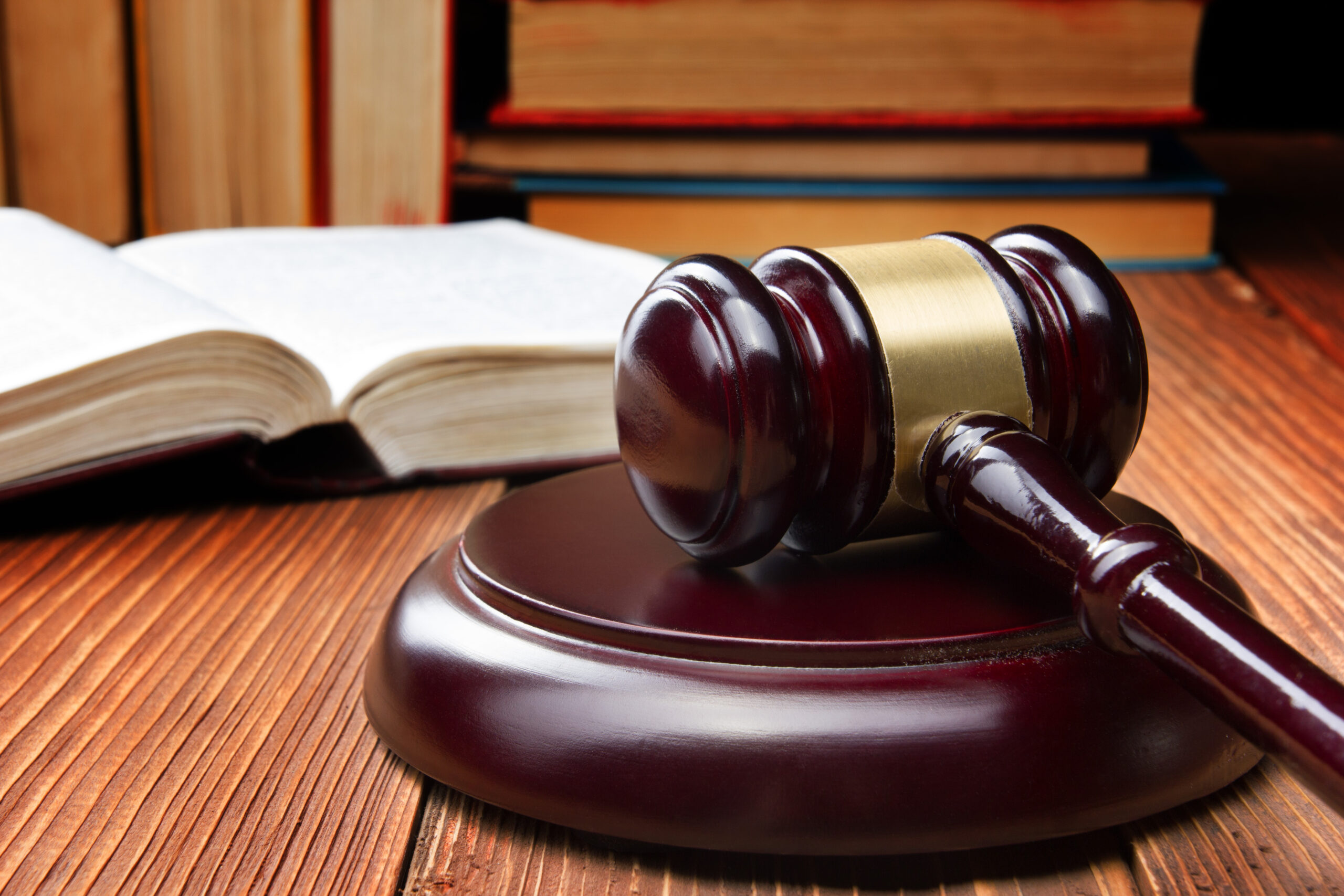 Wooden judge's gavel resting on a sound block atop a polished desk, with several open and stacked books in the background, symbolizing legal proceedings, justice, or litigation.