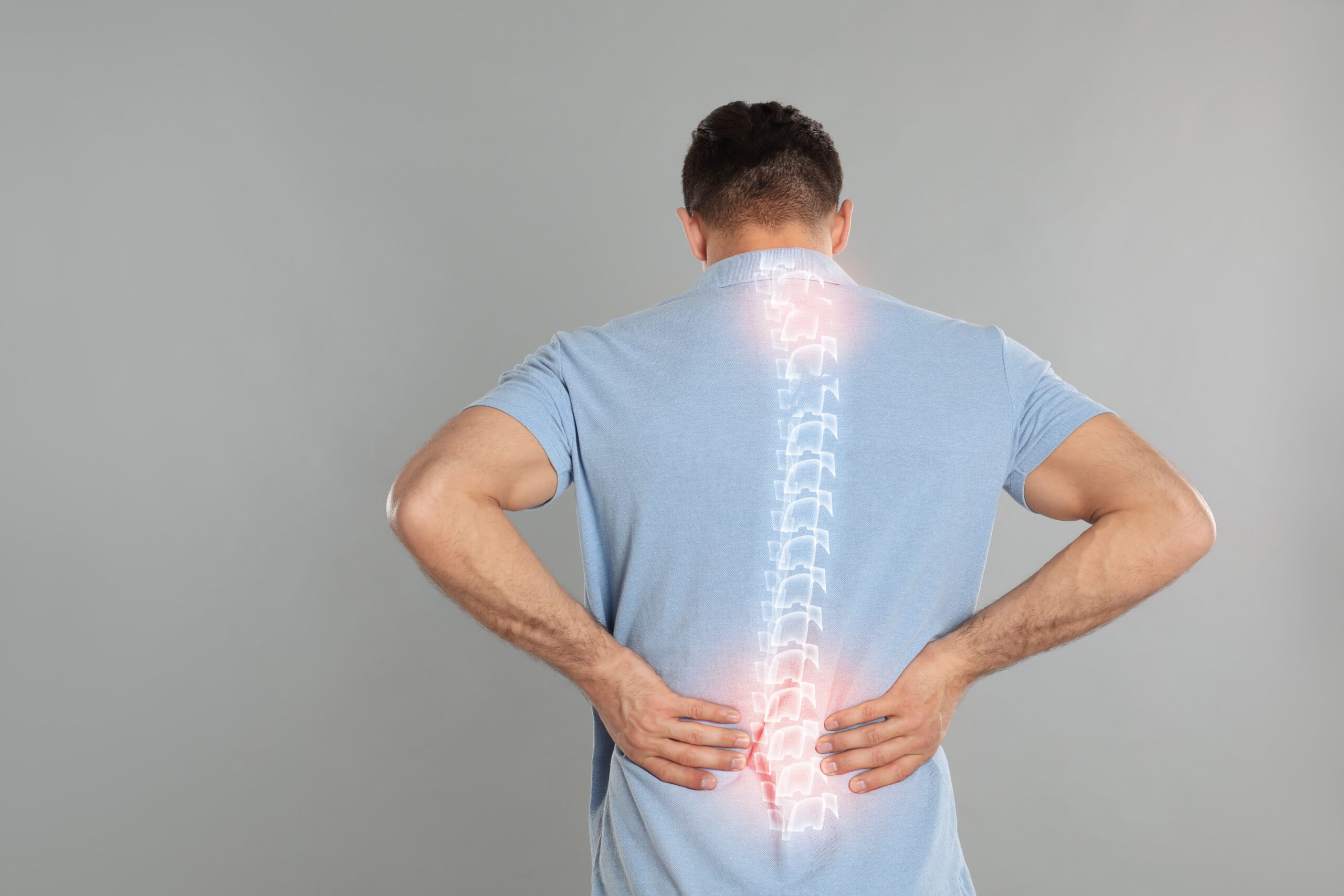 Illustration of a person viewed from behind holding their lower back, with a highlighted spine and glowing red area indicating lower back pain or discomfort in the lumbar region.