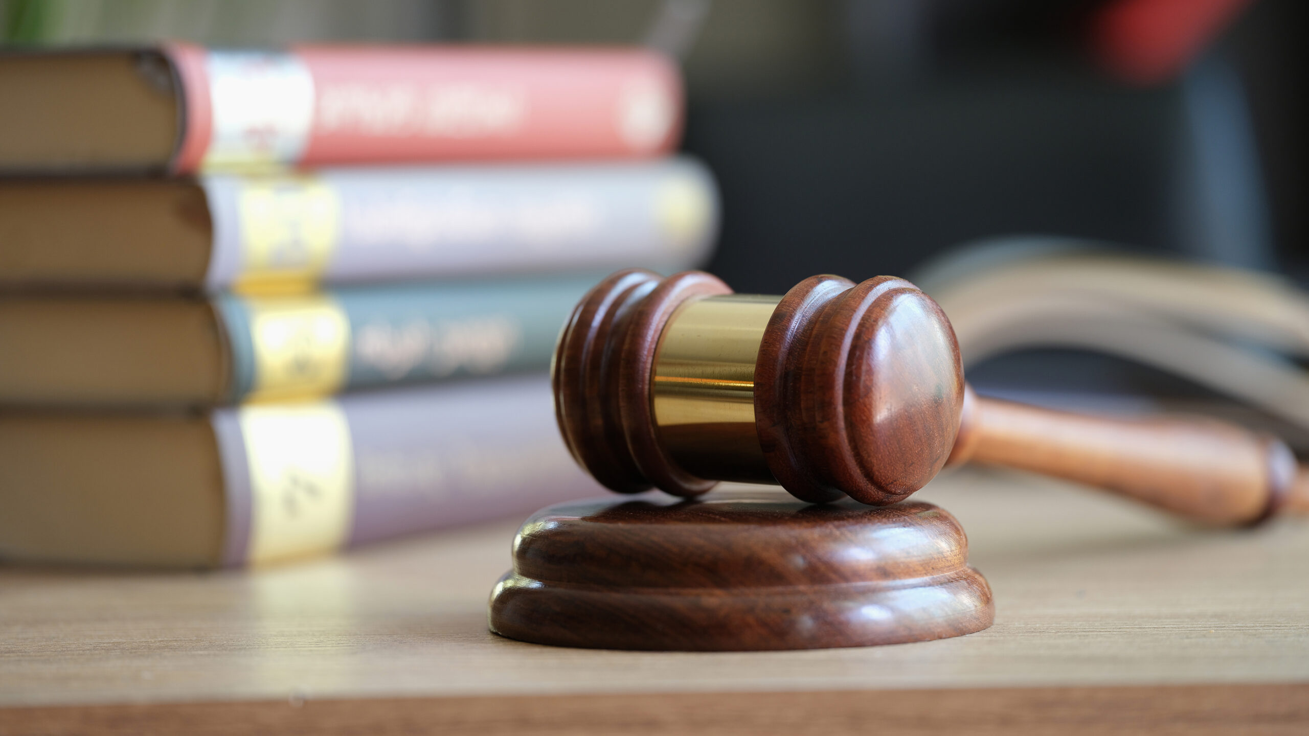 Wooden judge’s gavel resting on a sound block in the foreground, with a stack of law books blurred in the background, symbolizing legal proceedings, litigation, or regulatory matters.