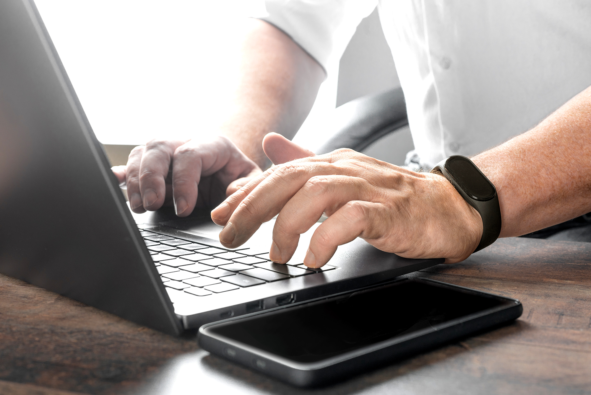 Person typing on a laptop at a desk with a smartphone nearby, representing digital communication or documentation.