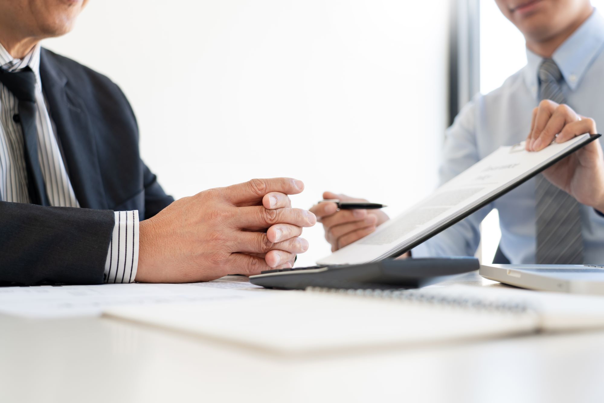Two professionals reviewing and signing paperwork across a desk during a meeting.