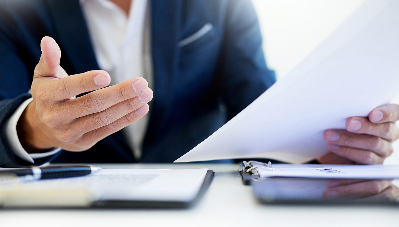 Business professional reviewing documents at a desk, with a tablet and clipboard visible nearby.