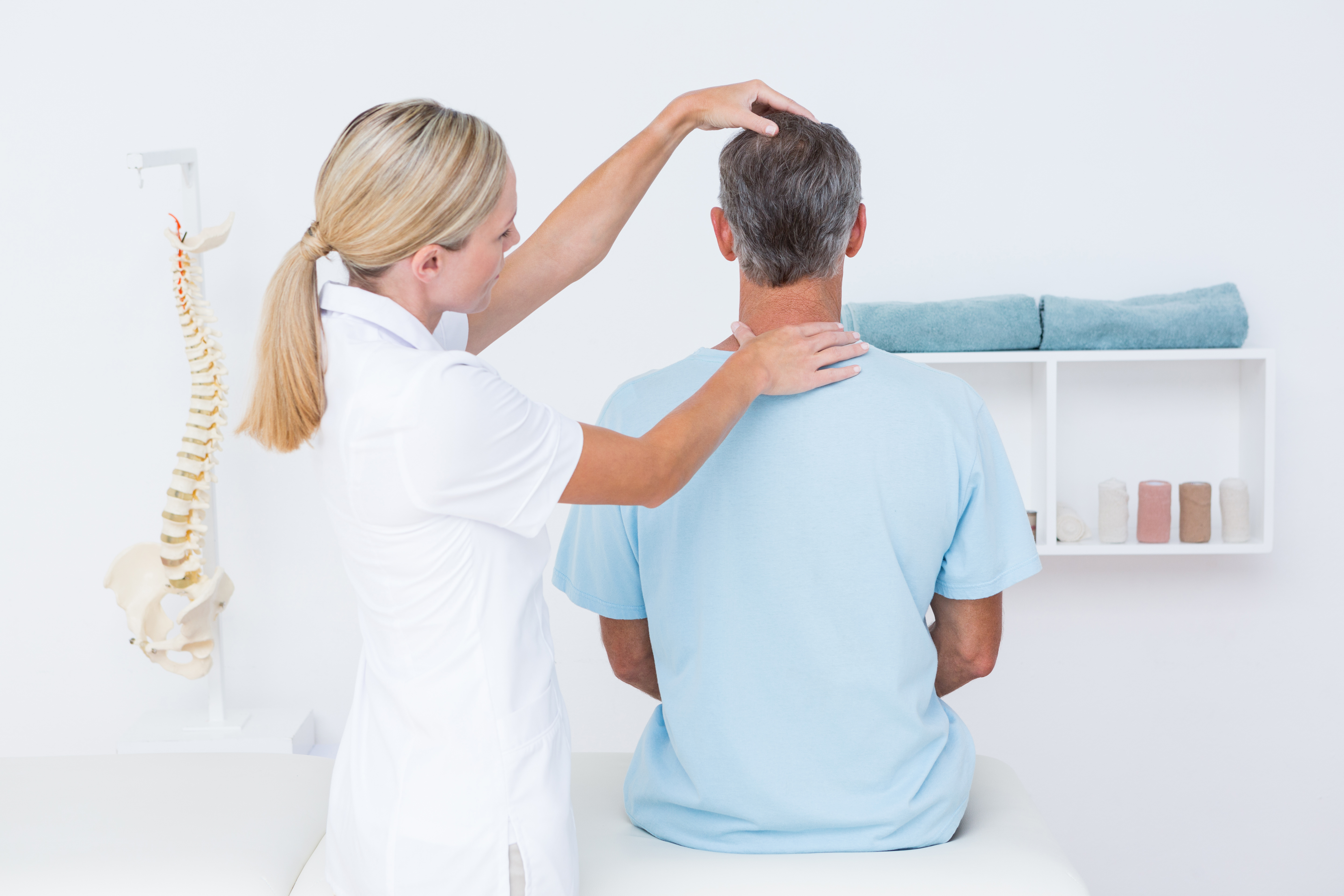 Chiropractor examining a seated patient's neck and upper spine in a clean chiropractic treatment room.