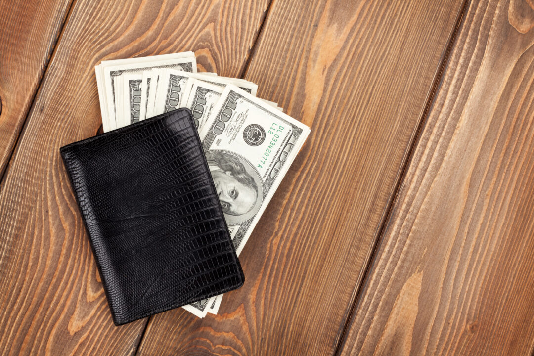 Black wallet with U.S. dollar bills on a wooden surface representing cash flow.