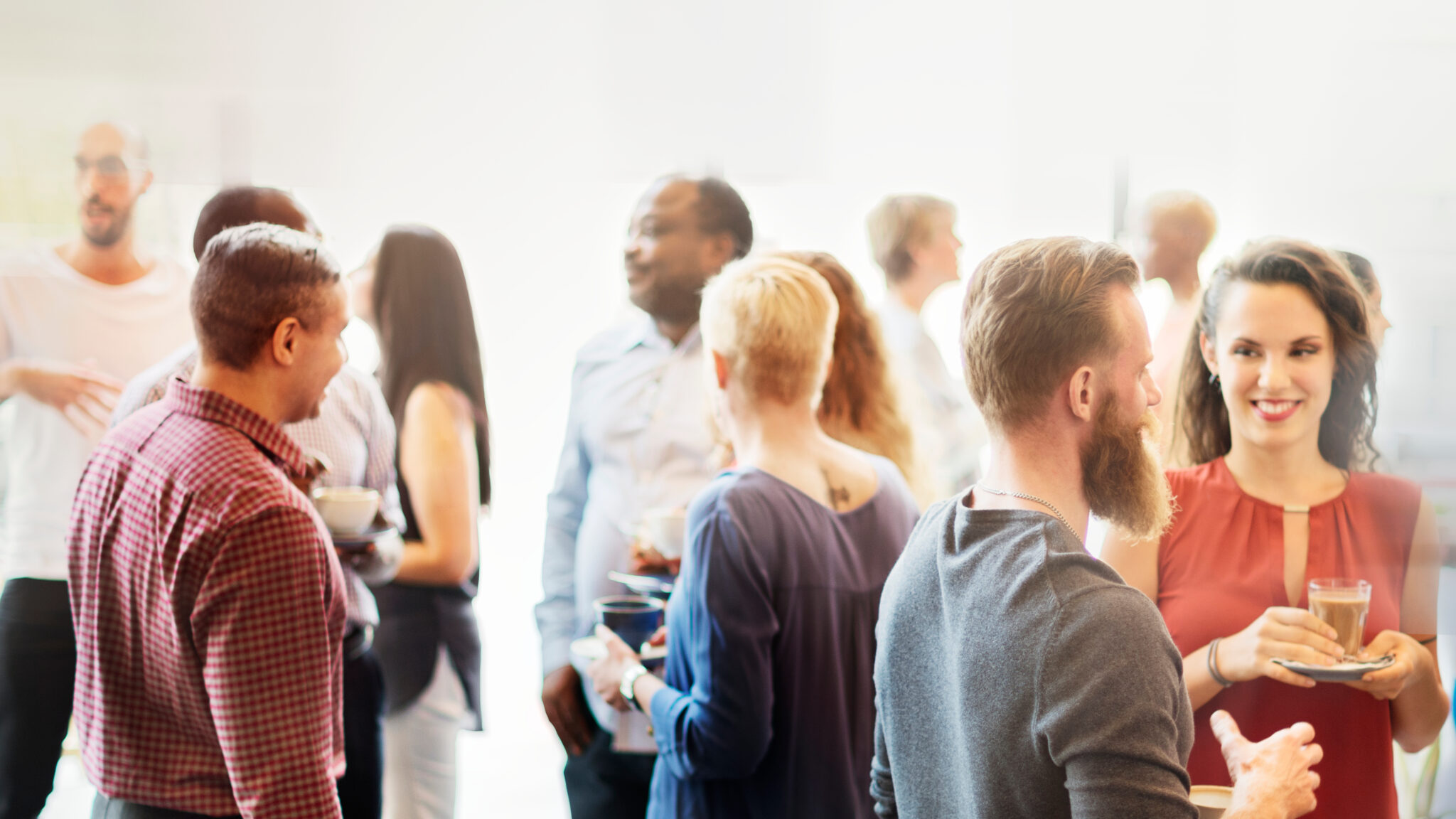 Professionals networking at a business event, talking in small groups in a bright conference setting.