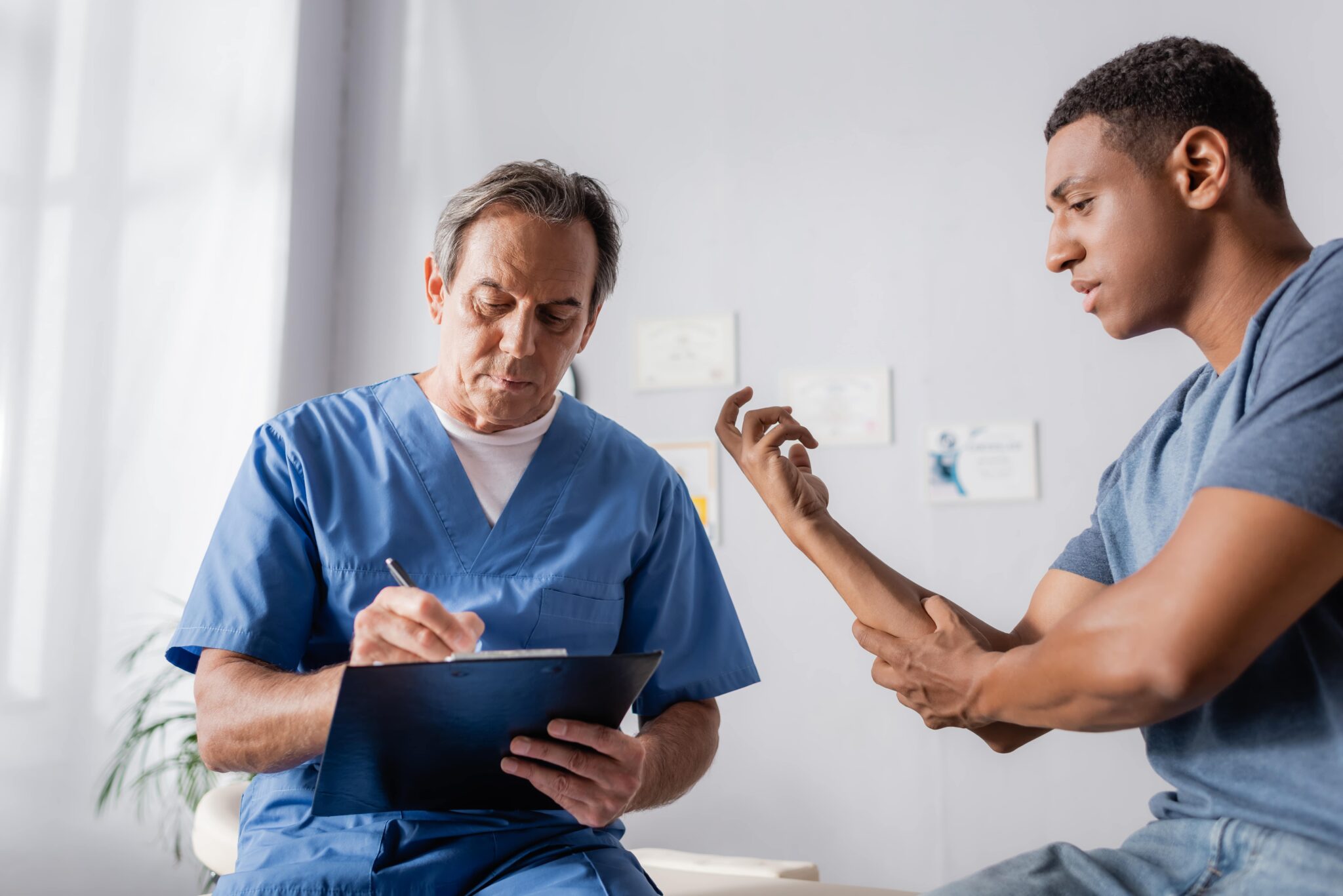 Healthcare professional reviewing notes on a clipboard while speaking with a patient in a clinical setting.