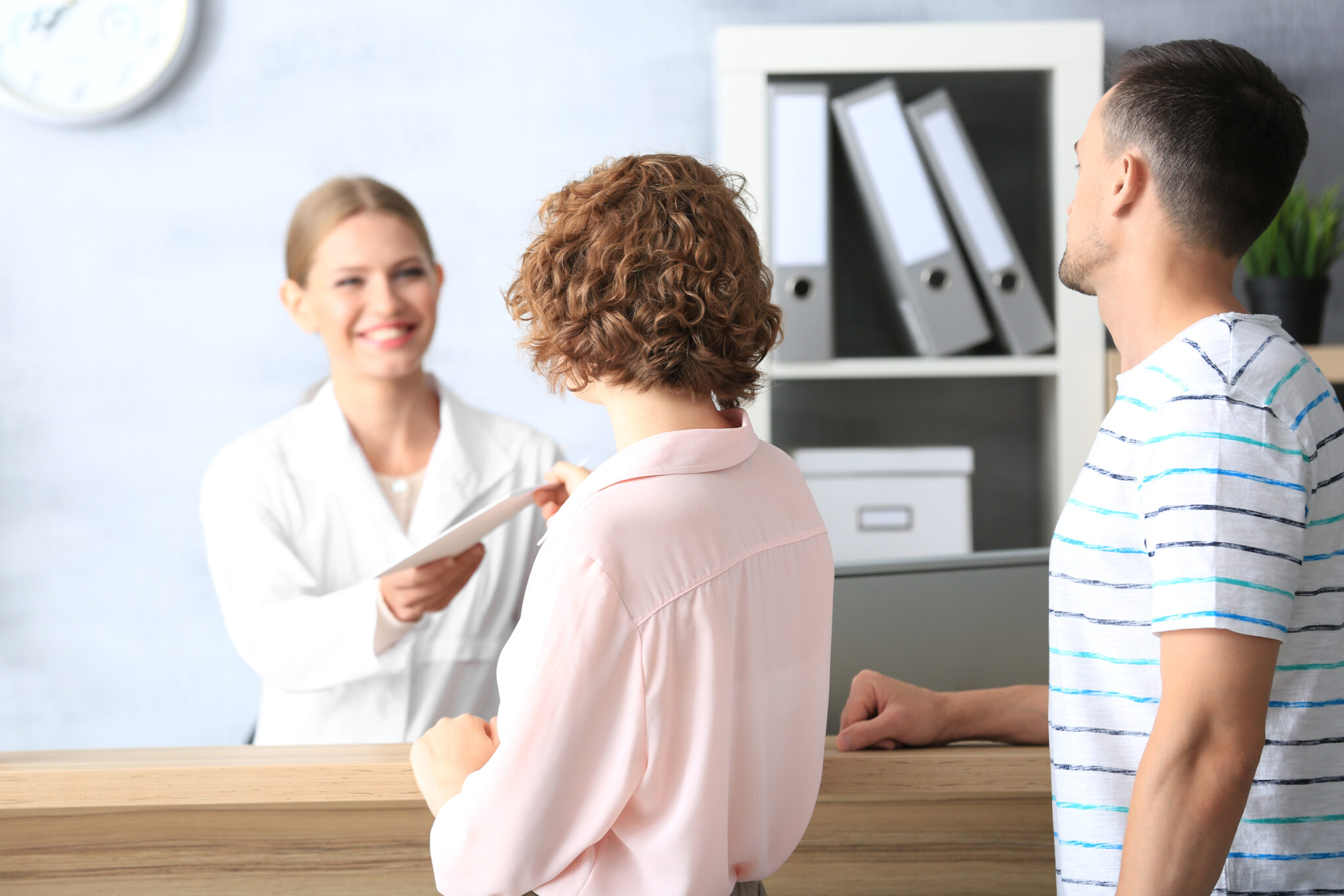 Healthcare professional hands a folder to two patients in a chiropractic office.