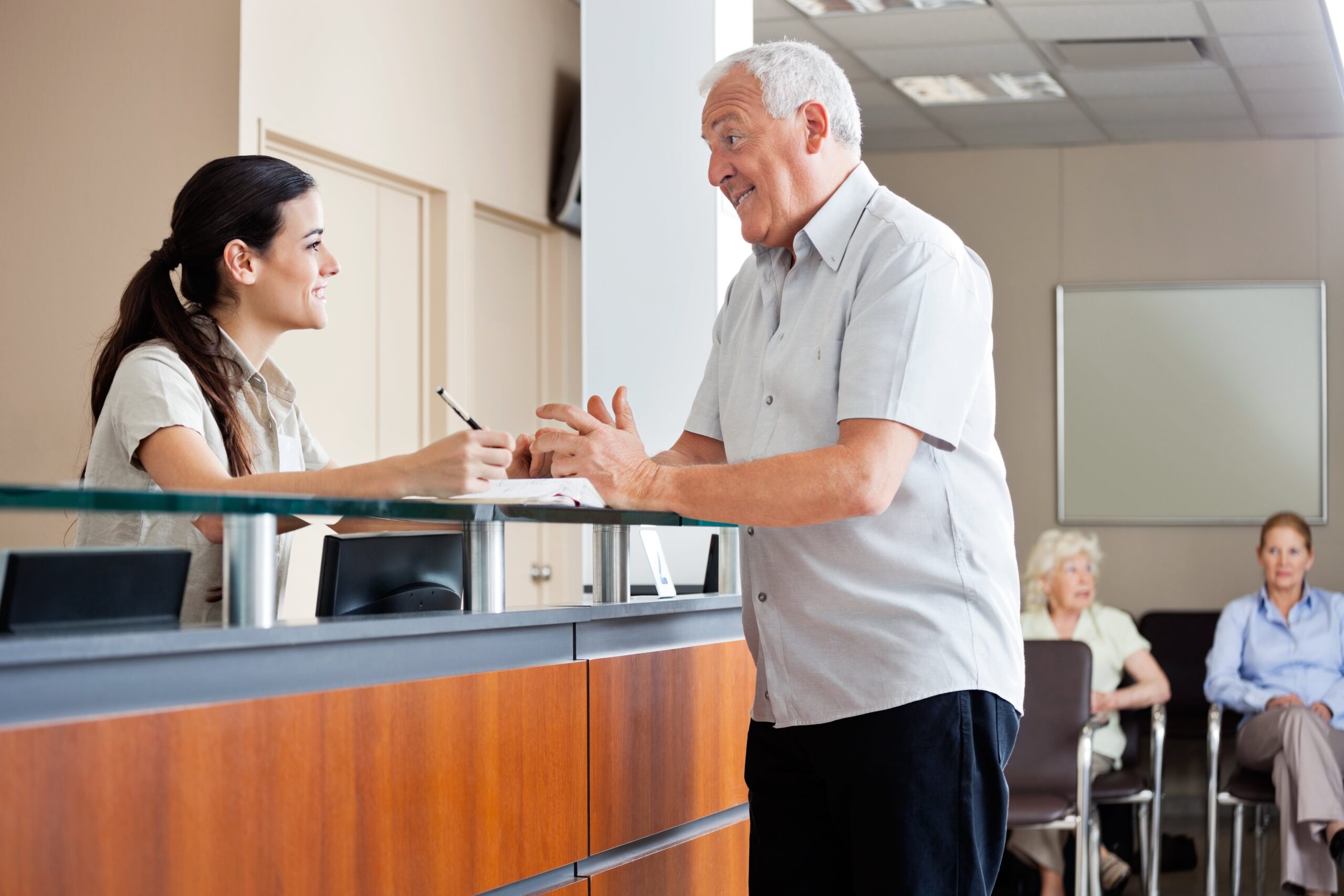 Older man communicating with woman at front desk.