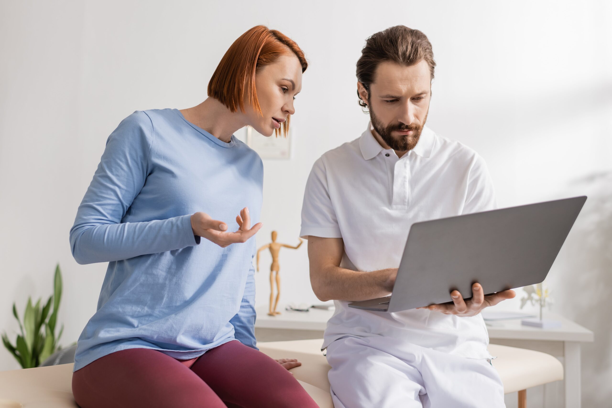 Chiropractor taking notes on laptop during exam.